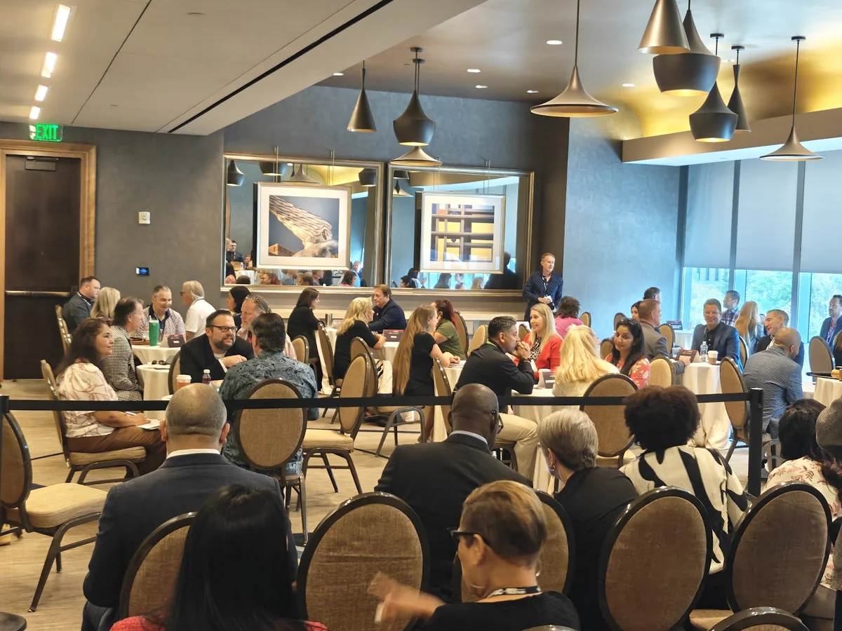 Attendees seated at round tables listening to a talk in an event room